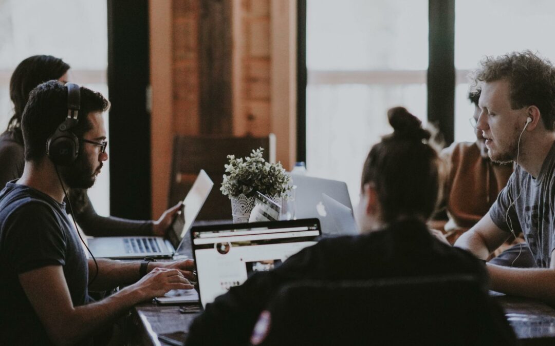 team of employees sit around a table working on computers