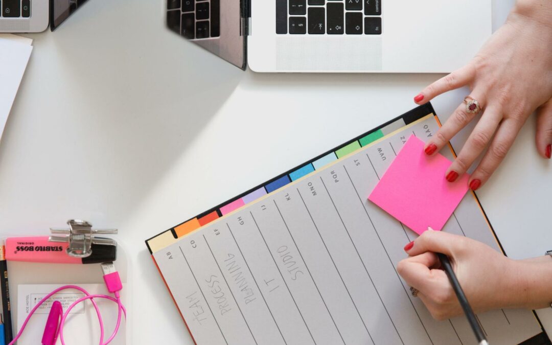 Person writing on a sticky note on top of an organized notebook.